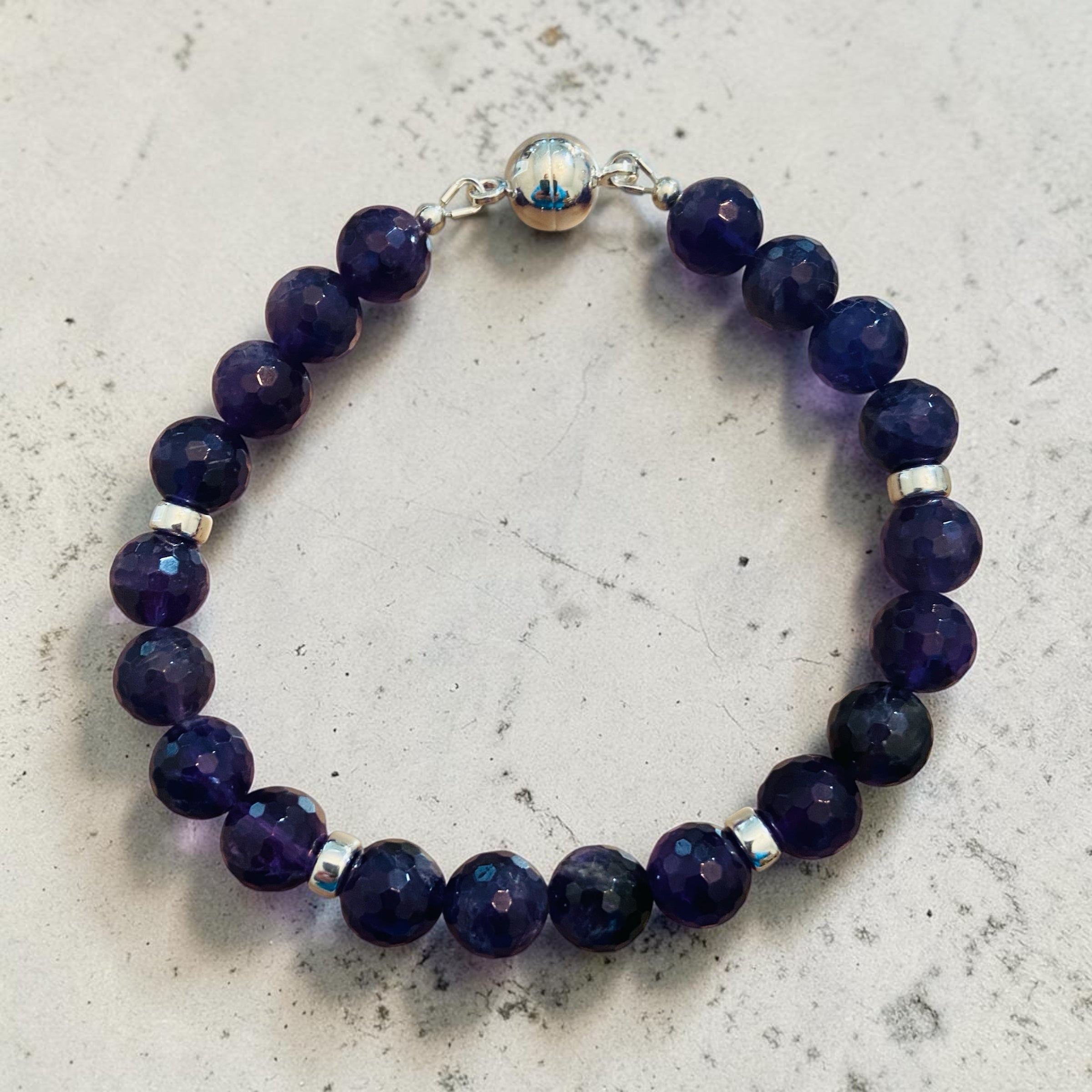 Amethyst beaded bracelet with silver accents on a light gray surface