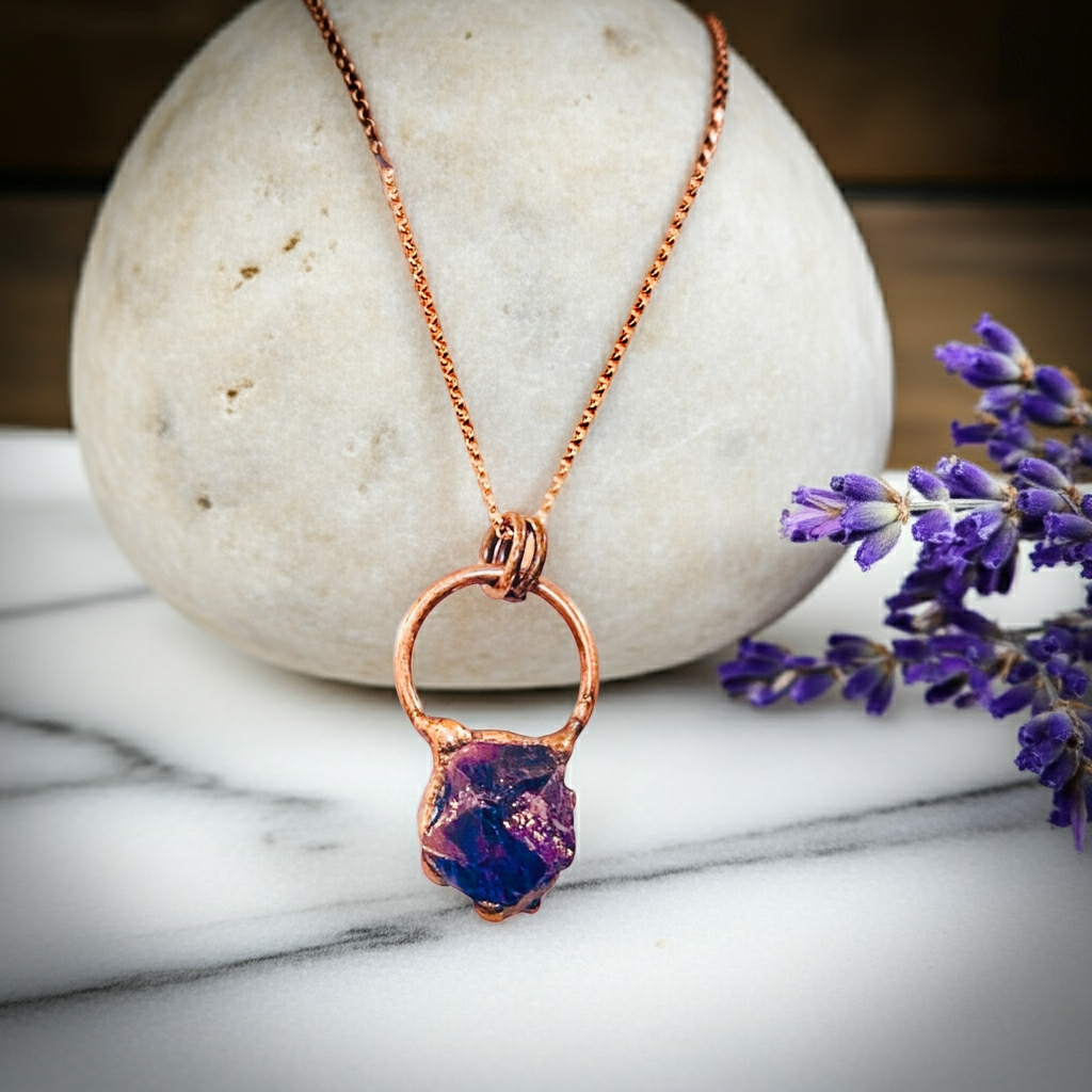 Copper necklace with a purple pendant on a marble surface with lavender flowers.