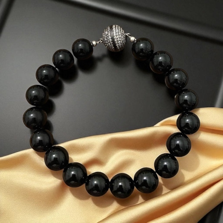 A beaded bracelet made of glossy black round beads, featuring a textured gunmetal-toned accent bead.
