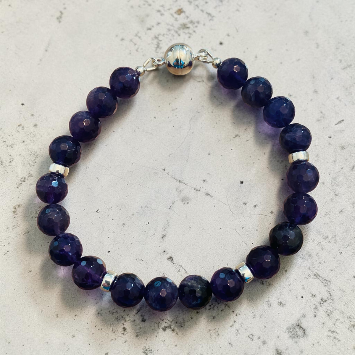 Amethyst beaded bracelet with silver accents on a light gray surface