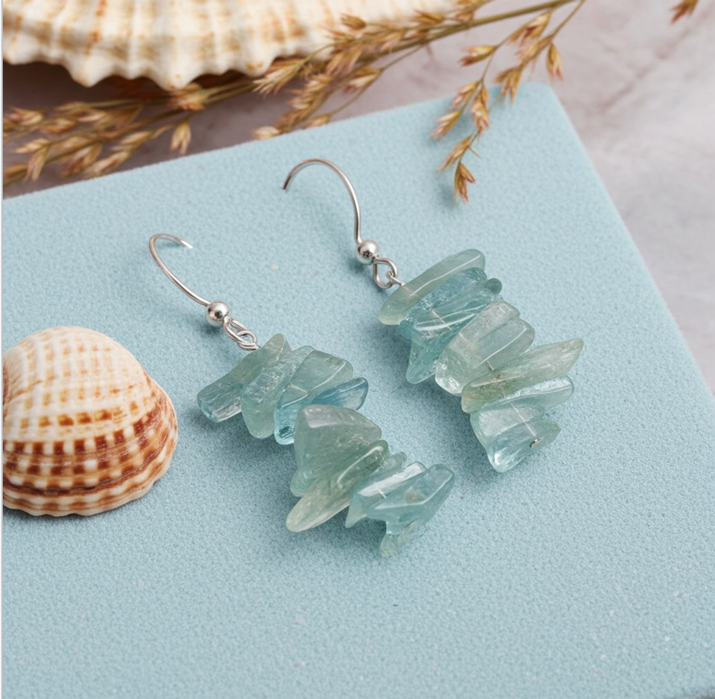 Pair of light blue stone earrings on a light blue surface with shells and dried grasses.