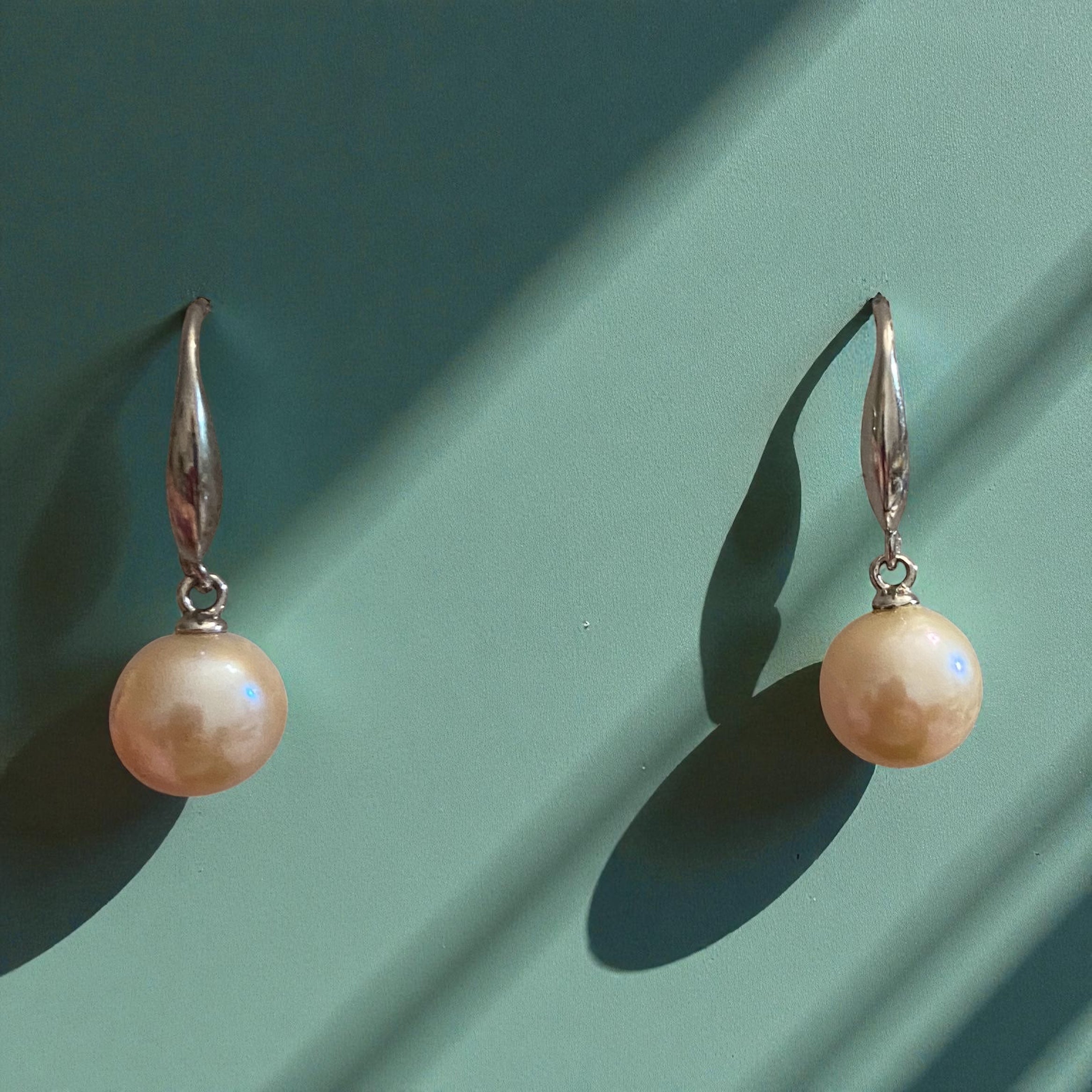 Pair of peach pearl earrings on a green background